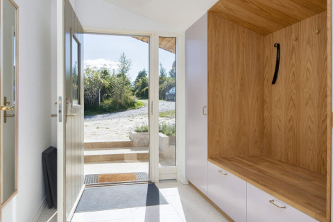 Ingang van een vakantiehuis in Rønde, Denemarken, met houten zitbank en zicht op het groen.