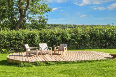 Terraza de madera con tres sillas y una mesa en casa vacacional de 4 estrellas en Rønde, Dinamarca.