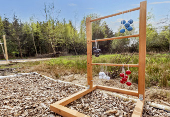 Udendørs spil ladder golf i træramme med farvede kugler, placeret i en natur omgivelser ved en lodge.