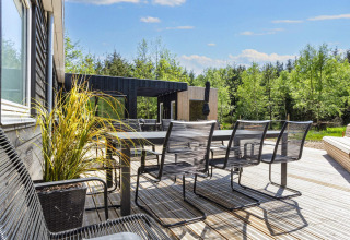 Terrasse extérieure avec table à manger et chaises près d’un gîte 5 étoiles à Øster Assels, forêt autour.