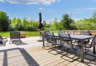 Terrasse med moderne havemøbler, liggestole og parasol i rolige grønne omgivelser ved Øster Assels.