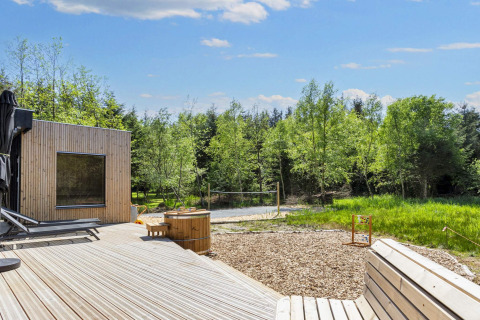 Udendørs terrasse med moderne træhytte, spabad og udsigt over natur og skov ved Øster Assels, Danmark.