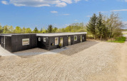 Moderne zwarte vakantiewoning in Øster Assels, Denemarken, met grindpad en bomen rondom.
