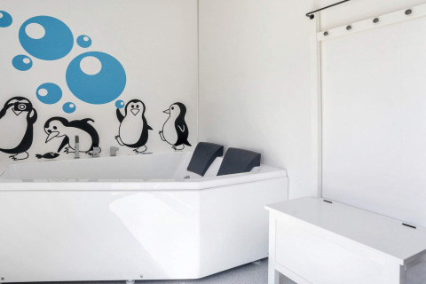 Salle de bain lumineuse avec baignoire blanche et décor mural pingouins et bulles à Øster Assels, Danemark.