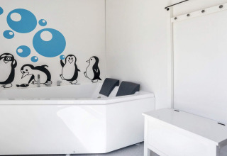 Lichte badkamer met wit bad, pinguïn- en blauwe bubbelstickers aan de muur in lodge Øster Assels.