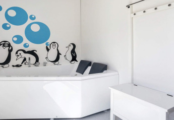 Bright bathroom with white bathtub, penguin wall art, and blue bubble decals at a lodge in Øster Assels.