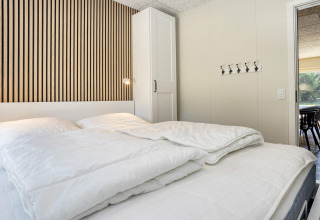 Camera moderna con parete a doghe in legno, armadio bianco e letto matrimoniale nella casa vacanza Øster Assels.