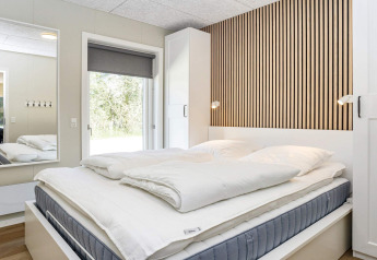 Chambre moderne avec mur à lames bois, lit double et grand miroir dans maison de vacances 5 étoiles à Øster Assels.