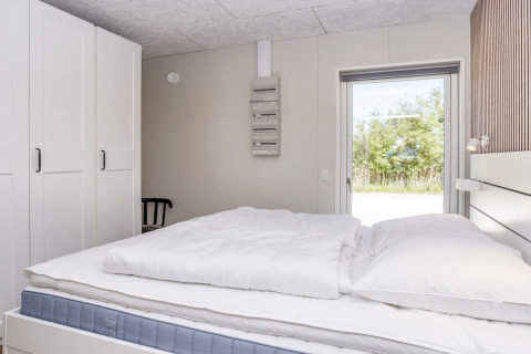Chambre lumineuse avec lit double, armoires et vue sur la nature dans une maison de vacances à Øster Assels.