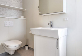 Modern bathroom with wall-mounted toilet, white sink, and mirror cabinet at a lodge in Øster Assels, Denmark.