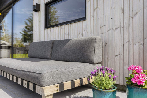 Buitensofa met grijze kussens en bloempotten bij een houten muur van 4-sterren vakantiehuis in Løgstør.