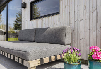 Sofá exterior con cojines grises y macetas junto a una pared de madera en una casa de vacaciones en Løgstør.