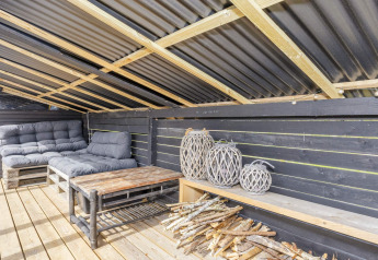 Overdekte loungehoek met bank, lantaarns en hout in een 4-sterren vakantiehuis in Løgstør, Denemarken.
