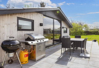 Terraza exterior de una casa de vacaciones en Løgstør, Dinamarca, con parrilla, mesa y sillas y césped.