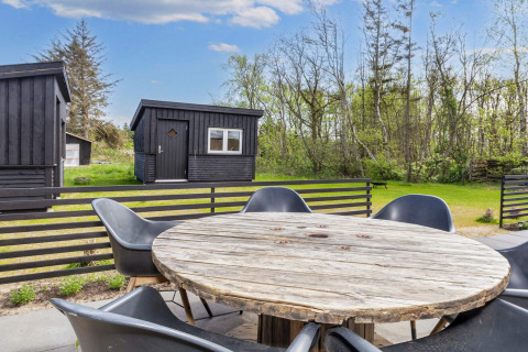 Área de asientos al aire libre con mesa redonda de madera y sillas negras en una casa de vacaciones en Løgstør.