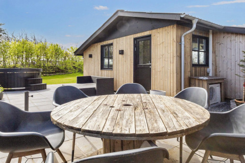 Patio esterno alla casa vacanze 4 stelle di Løgstør, Danimarca, con tavolo, sedie e vasca idromassaggio.