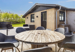 Außenterrasse am 4-Sterne-Ferienhaus in Løgstør, Dänemark, mit Holztisch, Stühlen und Whirlpool.