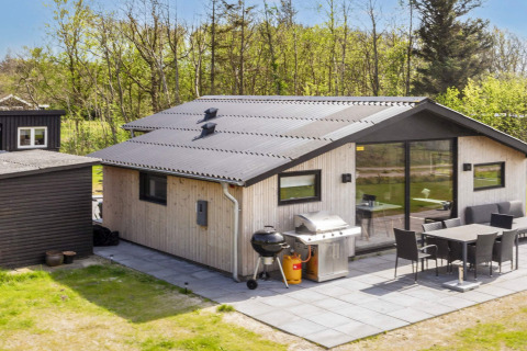Terrasse am 4-Sterne-Ferienhaus in Løgstør, Dänemark, mit Grill, Esstisch und schöner grüner Kulisse.