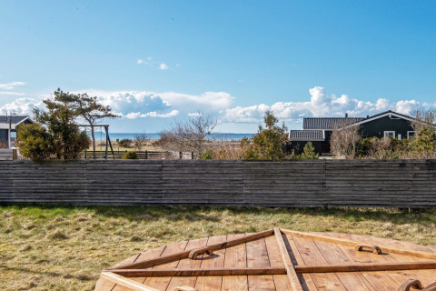 Zicht vanuit vakantiehuis in Løgstør, Denemarken, met houten omheining, tuin, zee en blauwe lucht.