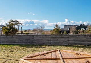 Vista dalla casa vacanze a Løgstør, Danimarca, con recinzione in legno, prato, mare e cielo sereno.