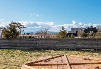 Blick vom Ferienhaus in Løgstør, Dänemark, mit Holzzaun, Garten, Meerblick und blauem Himmel.