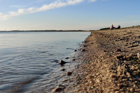 Strandbillede ved 4-stjernet feriehus i Løgstør, Danmark, med roligt vand og himmel ved solnedgang.