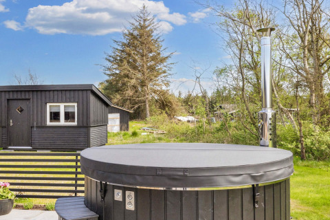 Außenaufnahme eines schwarzen Ferienhauses mit überdachtem Whirlpool im grünen Løgstør, Dänemark.