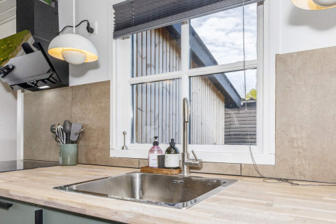 Fregadero moderno de cocina con grifo de acero y vista desde ventana a edificio de madera en Løgstør.