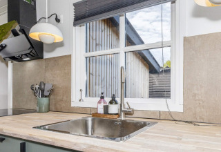 Évier de cuisine moderne avec robinet en acier et vue sur un bâtiment en bois à Løgstør, Danemark.