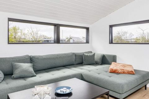 Salon moderne d’une maison de vacances 4 étoiles à Løgstør, Danemark, avec canapé vert et fenêtres.
