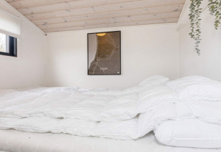 Slaapkamer in vakantiehuis in Løgstør, Denemarken, met wit beddengoed, wandkaart en houten plafond.