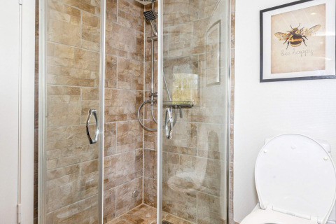 Badkamer met betegelde douche, glazen deuren en toilet in een vakantiehuis in Løgstør, Denemarken.
