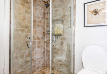 Salle de bain avec douche carrelée, portes vitrées et toilettes dans une maison de vacances à Løgstør, Danemark.