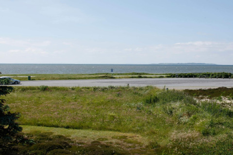 Uitzicht vanaf een lodge in Løgstør, Denemarken, met grasvelden, parkeerplaats en zee op de achtergrond.