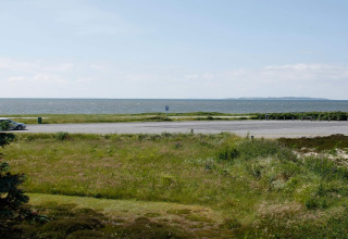 Vista da un alloggio a Løgstør, Danimarca, con prato verde, parcheggio e mare sullo sfondo.