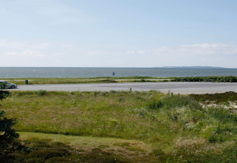 Vista desde una casa de vacaciones en Løgstør, Dinamarca, con césped, estacionamiento y el mar al fondo.