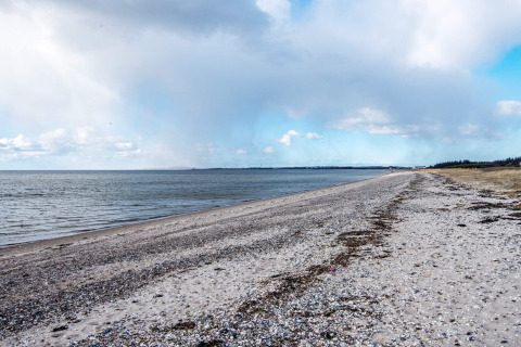 Ampia veduta di una spiaggia di ciottoli a Løgstør, Danimarca, con mare calmo e cielo nuvoloso.