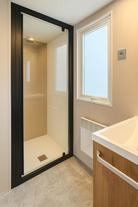 Moderne badkamer in een vakantiewoning op Camping Papillon in België met glazen douche en houten meubel.
