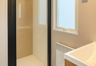 Moderne badkamer in een vakantiewoning op Camping Papillon in België met glazen douche en houten meubel.