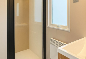 Modern bathroom in a holiday home at Camping Papillon in Belgium with glass shower, window, and wood vanity.