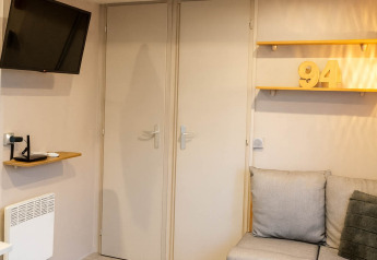 Stue i feriehus med moderne sofa, to borde, vægmonteret tv og dekoration med tallet 94 på Camping Papillon.