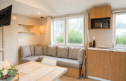 Sala de estar y cocina moderna en Holiday home (PL. 94) en Camping Papillon, Bélgica, con gran sofá y ventanales.