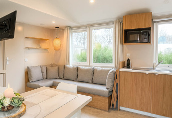 Soggiorno moderno e cucina in Holiday home (PL. 94) al Camping Papillon in Belgio con grandi finestre e divano ad angolo.