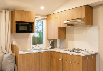Moderne vakantiekeuken met houten kasten, gasfornuis en magnetron in Camping Papillon, België.