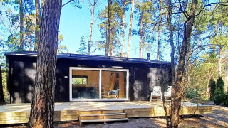 Moderne zwarte blokhut in het bos met terras, 4-sterren vakantiewoning in Höllviken, zonlicht.