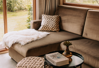 Moderne stue med knækket sofa, pude og faux pelsplaid i Klapkot-hytte, De Achterste Hoef, Holland.