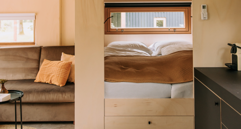 Lyst og hyggeligt interiør i en moderne hytte med sofa, seng og vinduer, der giver naturligt lys.