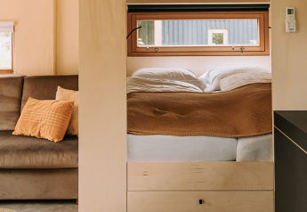 Interno di una cabina moderna e luminosa con divano grigio, letto accogliente e finestre soleggiate.