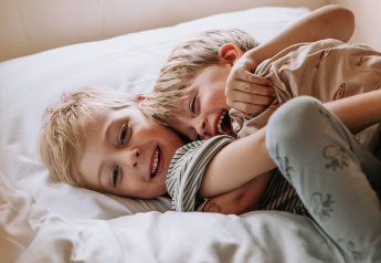 Twee vrolijke kinderen knuffelen en lachen samen op een bed in een knusse hut, genietend van het moment.
