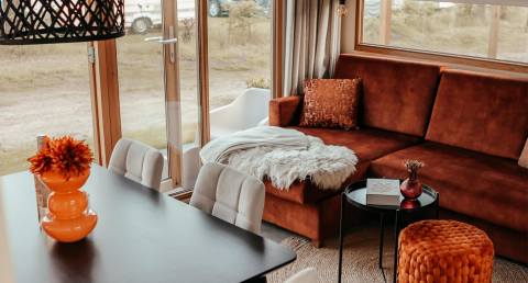 Acogedora sala en la cabaña Klapkot con sofá marrón, manta suave, mesa de comedor y amplios ventanales.